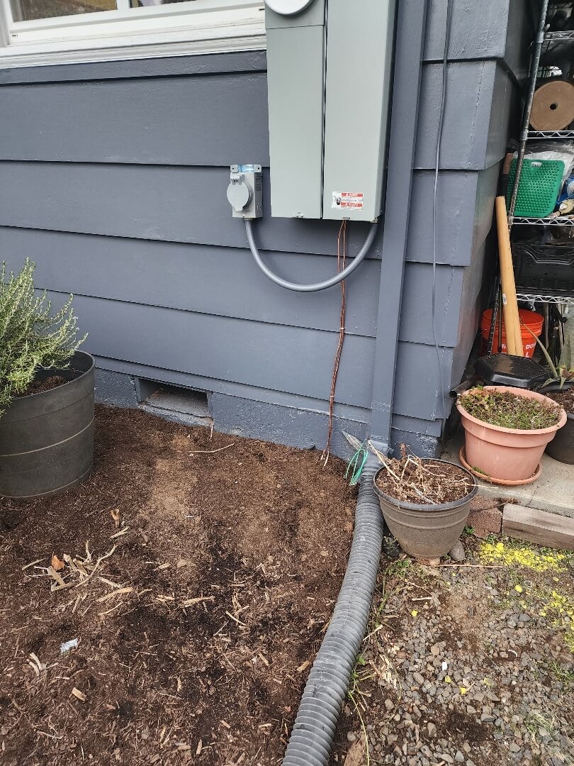 Exterior electrical meter and panel mounted on home siding with conduit and grounding near foundation