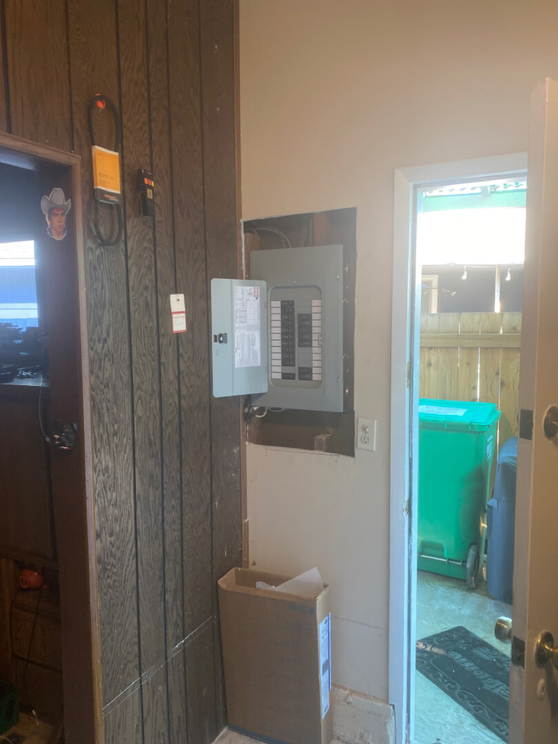 Basement electrical panel installed on wood wall near doorway with utility area in background