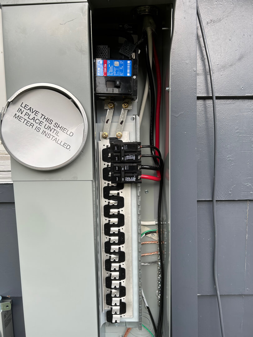 Open electrical panel showing breakers, wiring, and meter connection installed on exterior wall