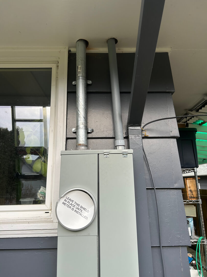 Exterior electrical panel with conduit lines running vertically along home siding near utility meter