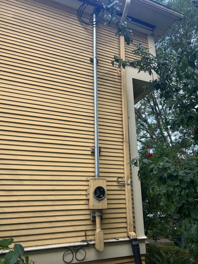 Service mast conduit running vertically along exterior siding up to roofline after repair in Portland OR