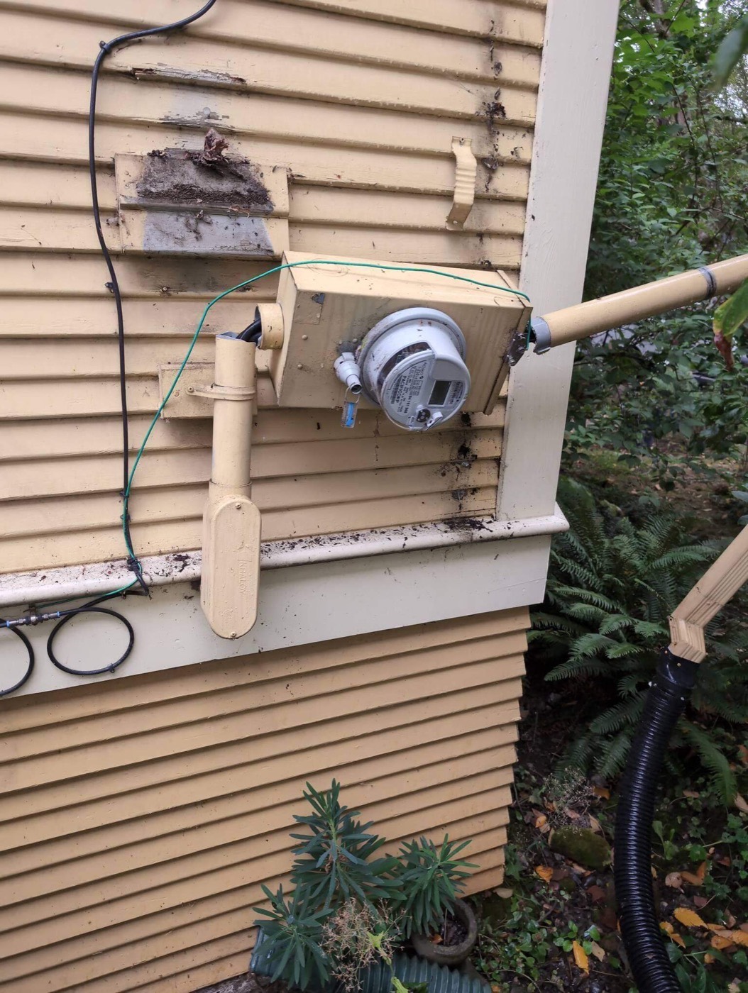 Damaged service mast and meter base with temporary support bracket on exterior wall in Portland OR