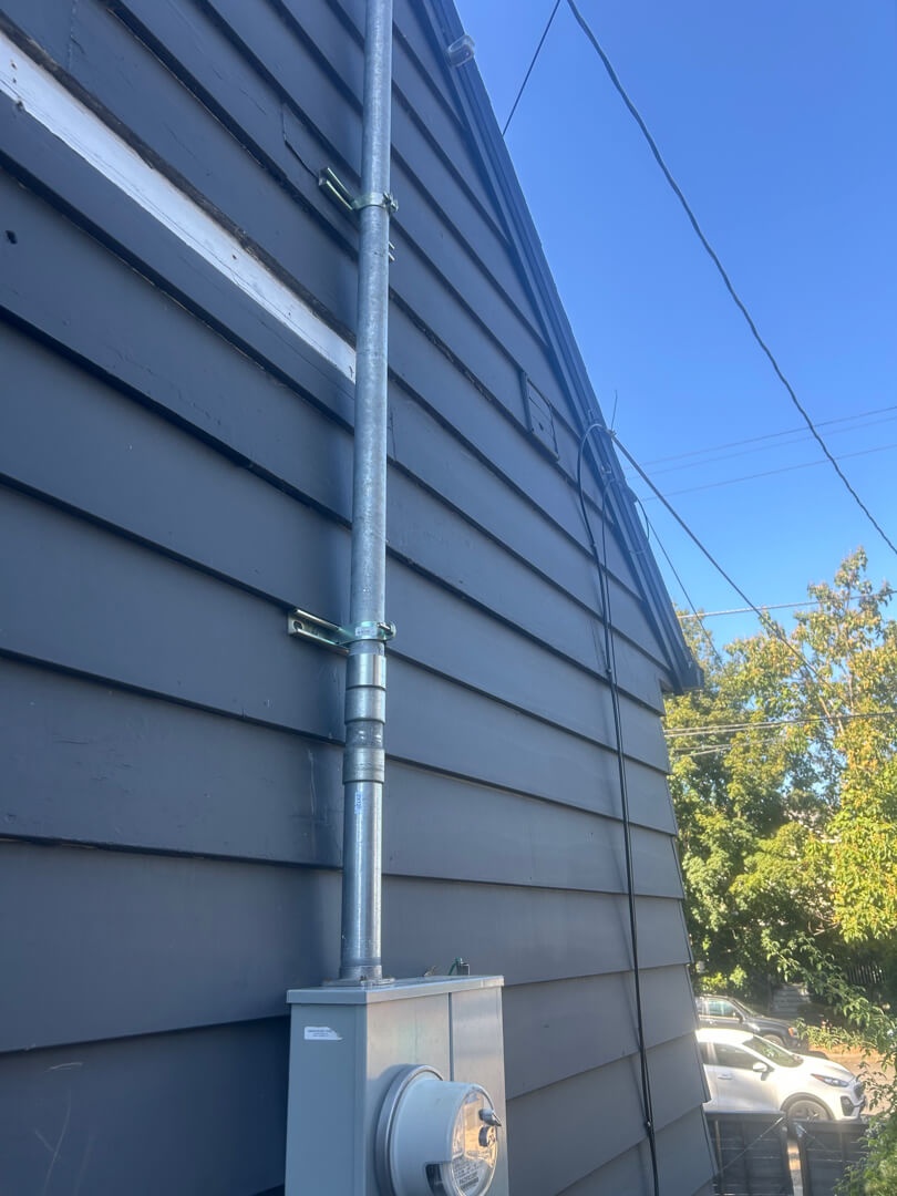 Exterior service mast conduit running vertically along siding connected to overhead utility lines in Portland OR