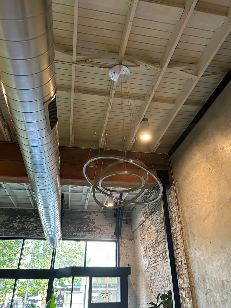 Industrial-style commercial space with high ceilings, exposed ductwork, and newly installed overhead lighting