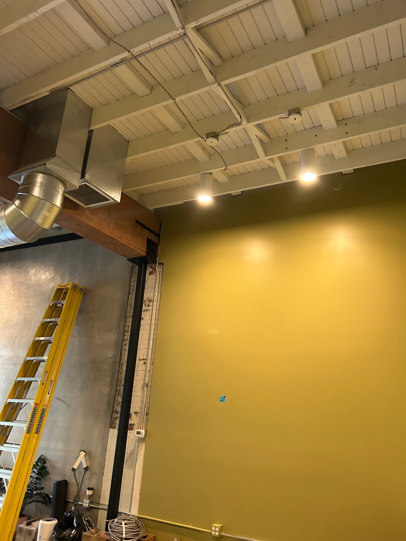 Commercial interior wall with overhead lighting installation and exposed ceiling structure in Portland OR