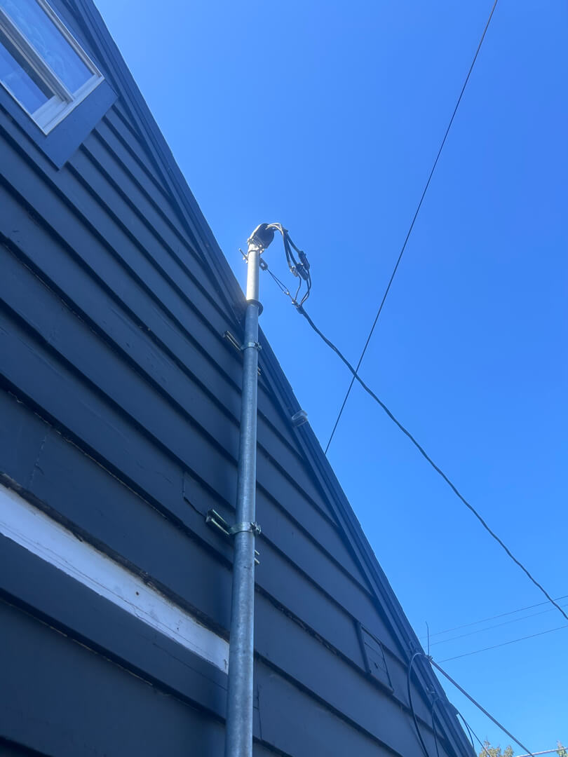 Electrical service mast pipe mounted along exterior wall extending above roofline to meet clearance requirements in Portland OR