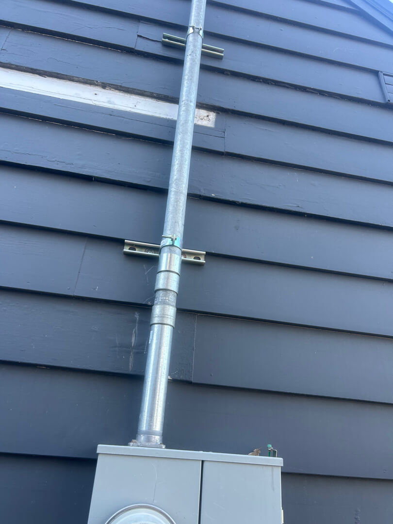 Service mast conduit secured to exterior wall with meter base ensuring proper support and clearance in Portland OR