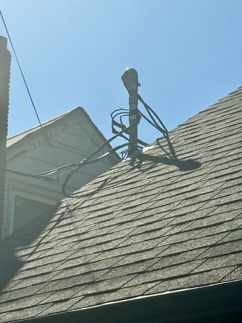 Electrician working on rooftop service mast pipe adjusting height and wiring for proper clearance in Portland OR
