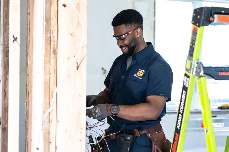 A Smiley Electric electrician wiring a service upgrade at a framed wall, tools on his belt.